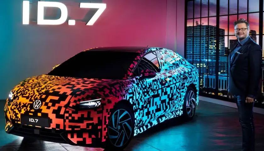 Nowy Volkswagen ID.7 prezentuje się w neonowym blasku, z efektownym wzorem QR kodu na karoserii. Obok stoi mężczyzna w garniturze, a w tle widać nocną panoramę miasta.