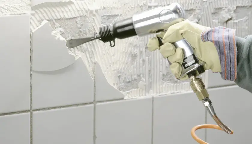 Mit einem Pressluftmeißel wird alter Fliesenkleber von der Wand entfernt.