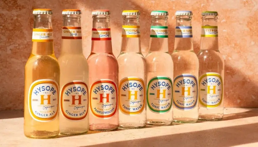 Sept bouteilles de bière et de tonic Hysopé alignées, avec des saveurs comme le gingembre et le pamplemousse, évoquant un apéritif en Italie.