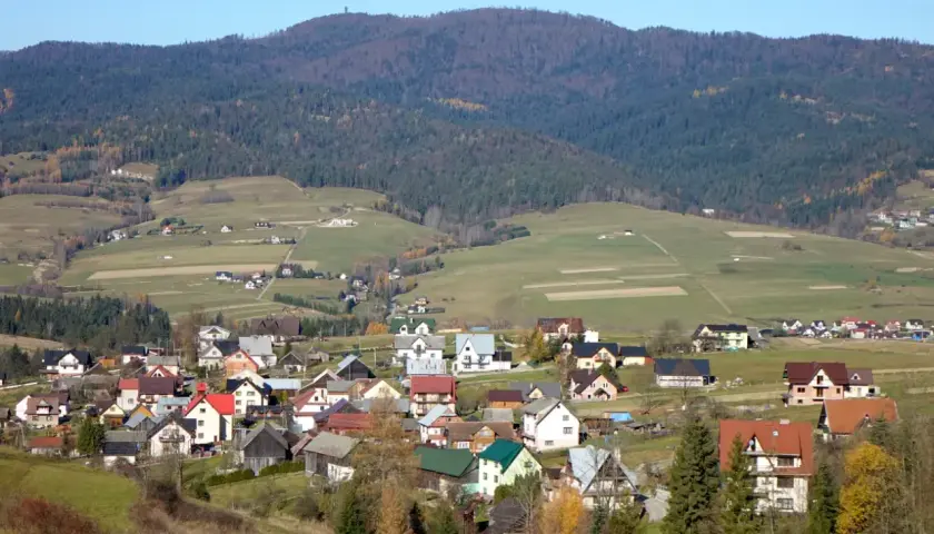 Widok na malowniczą wieś u podnóża góry, z której roztacza się widok na **Lubań szczyt**. Domy z czerwonymi dachami wtopione w zielone wzgórza.