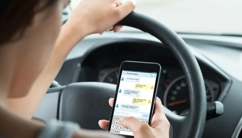 Person håller en telefon i bilen och skriver ett meddelande.