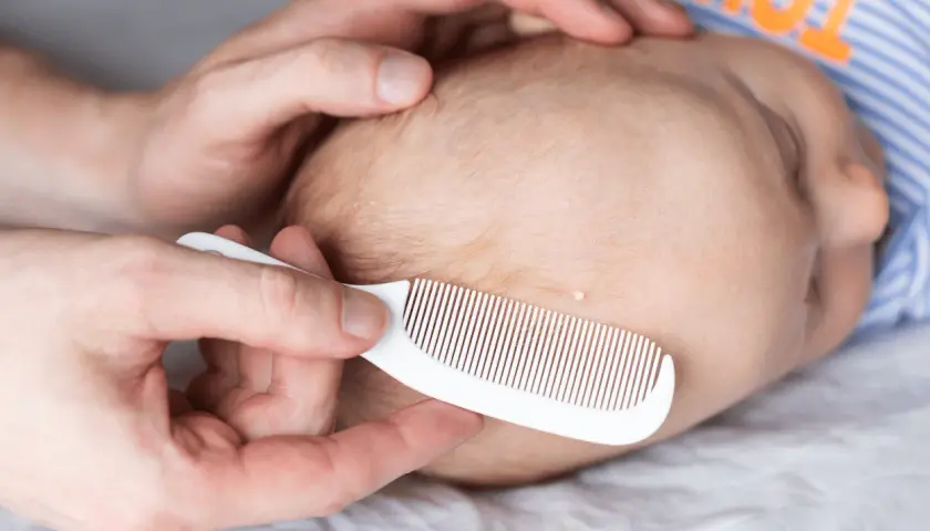 Delikatne czesanie główki niemowlęcia białym grzebykiem, by usunąć łuski ciemieniowe (cradle cap).