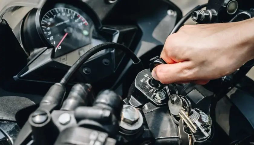 Mano girando la llave de contacto de una moto, pero no enciende. El tablero y las llaves están visibles.