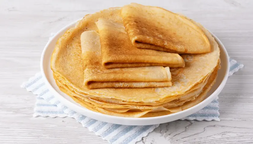 Pile de crêpes dorées, certaines pliées, sur une assiette blanche. Un délice sans oeuf pour un petit-déjeuner léger.