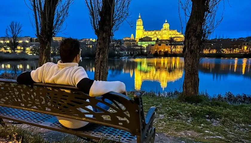 Persona sentada en un banco contempla la Catedral de Salamanca iluminada al anochecer, reflejada en el río. Ideal para saber qué ver en Salamanca en un día.
