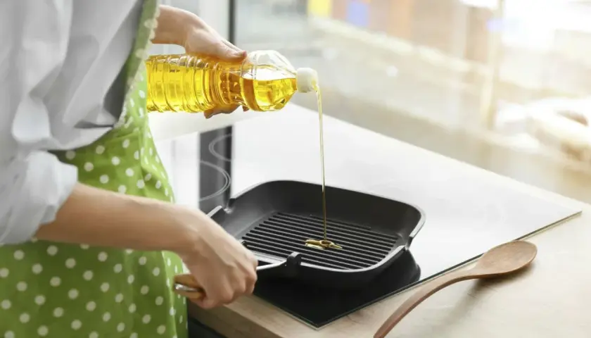 En person häller vegetabilisk olja i en grillpanna.