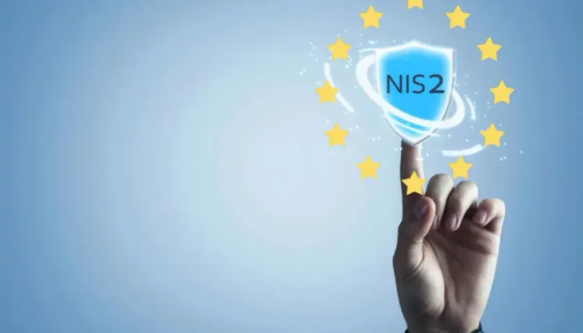 Palec wskazujący dotyka tarczy z napisem NIS2, otoczonej gwiazdkami Unii Europejskiej. Symbolizuje to bezpieczeństwo i zgodność z dyrektywą NIS2.