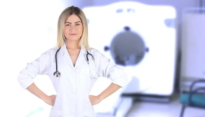 Uśmiechnięta rejestratorka medyczna w białym kitlu ze stetoskopem, na tle aparatu RTG. Zastanawiasz się, ile zarabia rejestratorka medyczna?