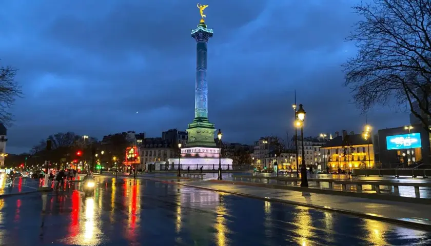 Wieczorny Paryż po deszczu. Kolumna Bastylii lśni w świetle latarni, a mokry asfalt odbija światła miasta.