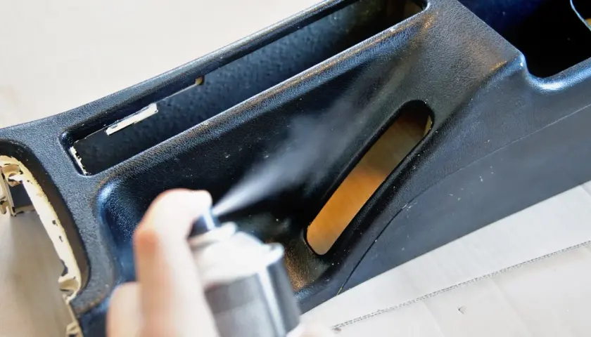Ręka trzyma puszkę z farbą w sprayu, wykonując malowanie plastików. Odświeżanie wnętrza samochodu.
