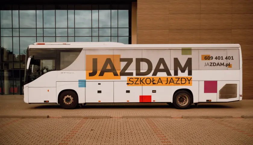 Biały autobus szkolny z napisem "JAZDAM SZKOŁA JAZDY" i numerem telefonu.