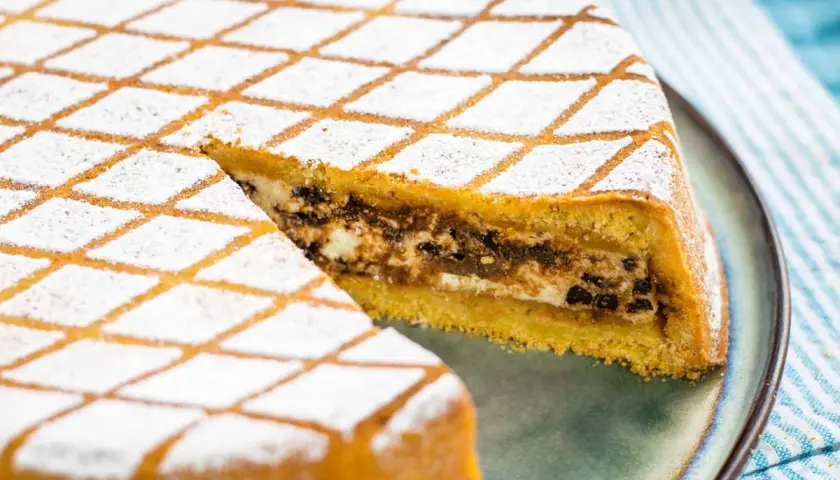Una fetta di cassata al forno, con la sua copertura a rombi di zucchero a velo, rivela un ripieno goloso di ricotta e cioccolato.