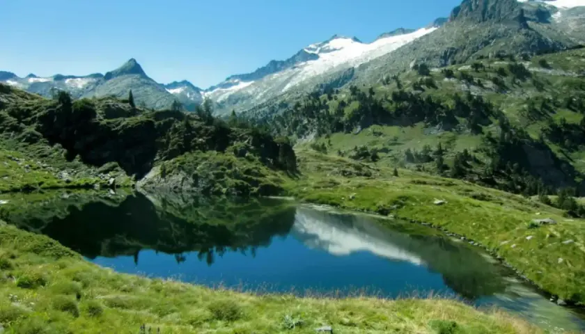 Reflejo de montañas nevadas en los ibones de Villamuerta, un paisaje alpino sereno.