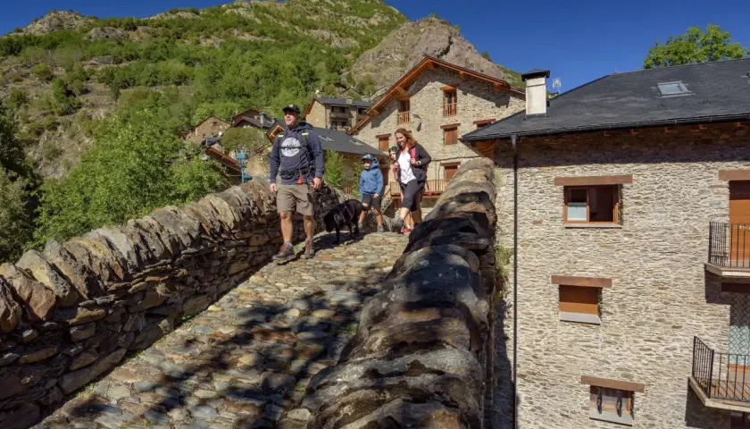 Familia pasea por un puente de piedra en un pueblo pirenaico, disfrutando de actividades al aire libre.