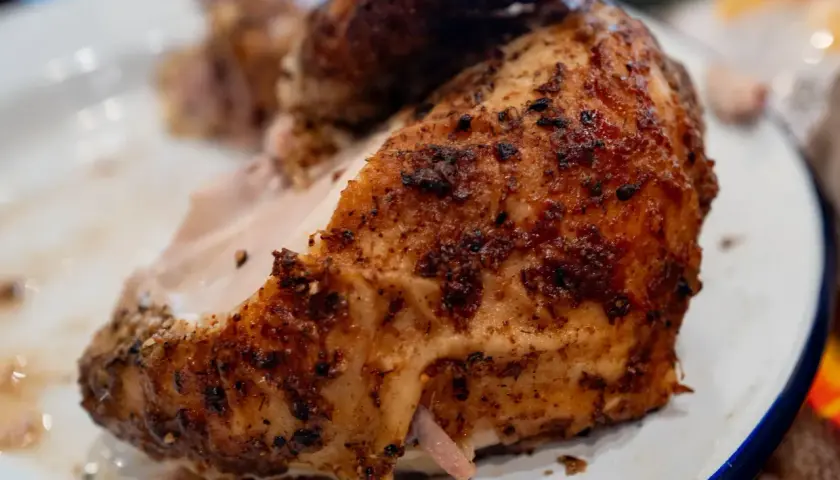Un morceau de poulet au four cuisson lente, doré et savoureux, servi sur une assiette blanche.