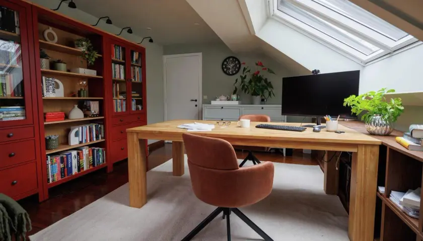 Accogliente angolo studio in mansarda con scrivania in legno, librerie rosse e lucernario.
