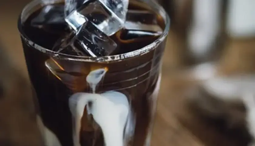 Ett glas med is och mörk, stark kaffe där grädde virvlar ner. En perfekt vietnamesisk iskaffe för en varm dag.