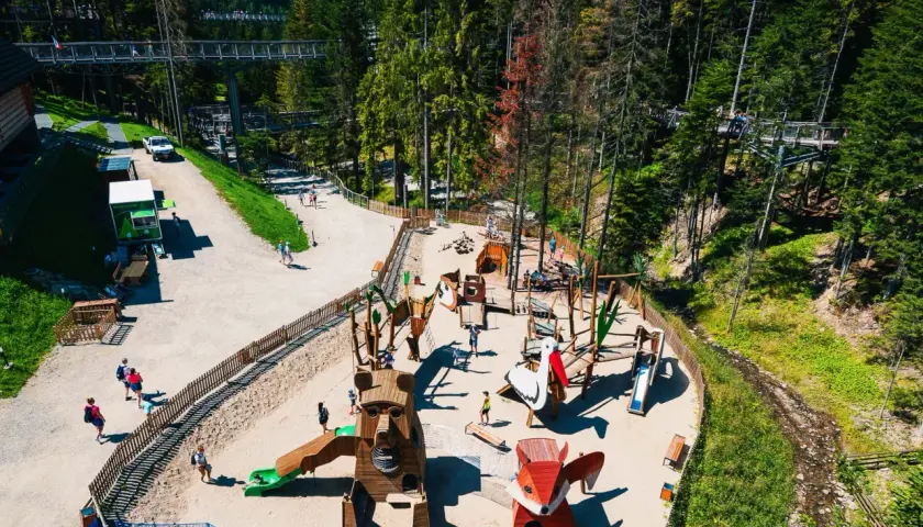 Wesołe miasteczko dla dzieci w centrum przyrodniczo-edukacyjnym Brama w Gorce. Drewniane zwierzątka, zjeżdżalnie i ścieżka w koronach drzew.