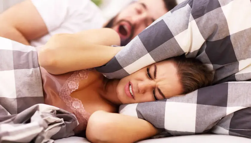 Donna stressata dall'apnea notturna del partner, si copre le orecchie con il cuscino.