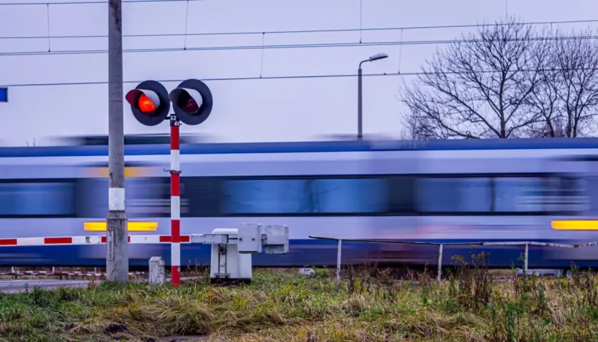 Pędzący pociąg mija przejazd kolejowy z czerwonymi światłami, zgodnie z nowym rozporządzeniem o przejazdach kolejowych.