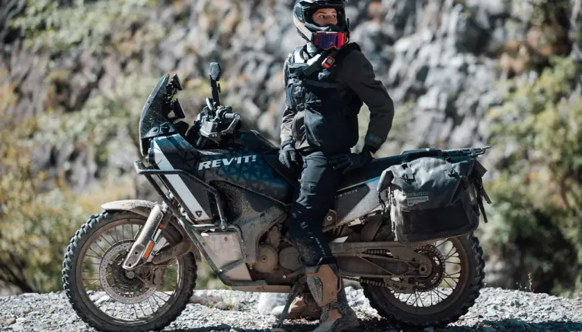Motociclista con equipo **waterproof** listo para la aventura. ¿Será **Gore-Tex**? La moto, su compañera en terrenos difíciles.