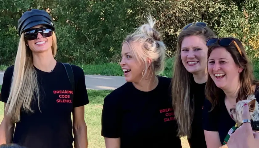 Paris Hilton och vänner ler glatt utomhus, alla bär svarta t-shirts med texten "Breaking Code Silence", som om de är med i en serie om sekt.