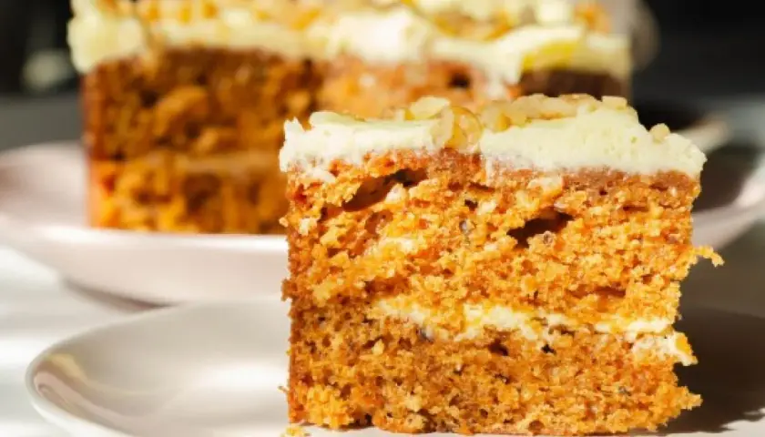 Wilgotne ciasto marchewkowe z kremowym lukrem, idealne na dietę. Pyszny kawałek na talerzyku.
