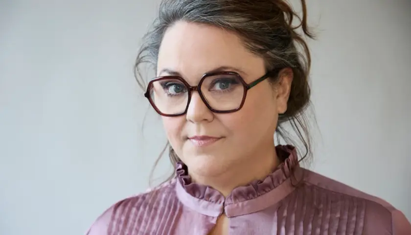 Malin Haawind med glasögon och en rynkad krage på en ljus bakgrund.
