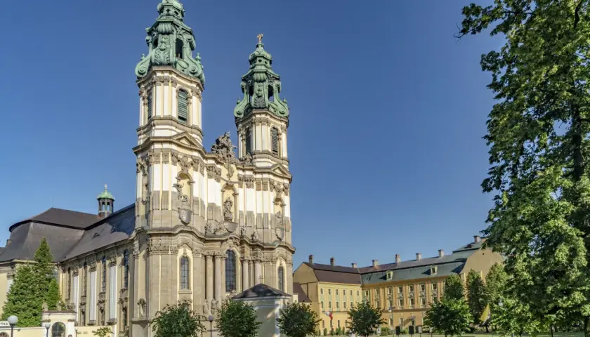 Barokowy zespół klasztorny w Krzeszowie z dwiema wieżami i rozległym skrzydłem, otoczony zielenią.