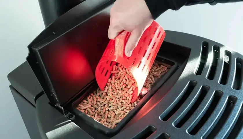 Ręka wsypuje pellet do zasobnika czarnego pieca na pellet.