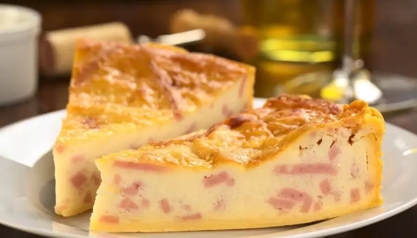Deux parts de quiche jambon fromage dorée sur une assiette blanche, avec un verre de vin en arrière-plan.