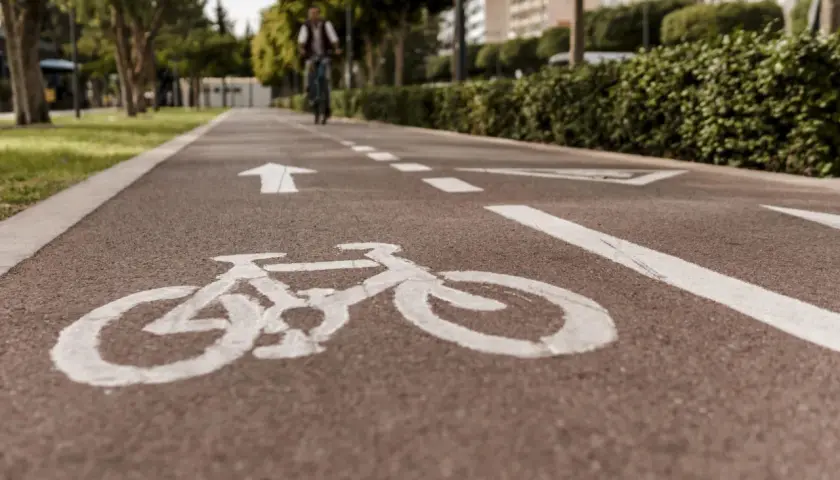Ścieżka rowerowa z białym znakiem P23 i strzałką kierunkową. W oddali widać rowerzystę.