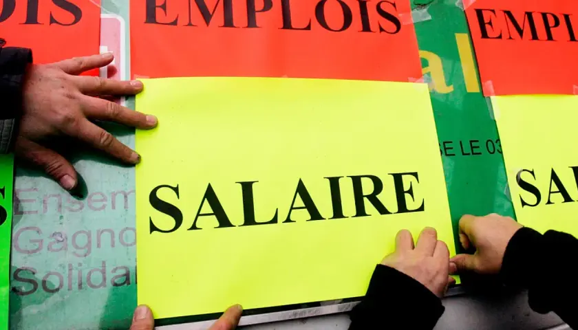 Ręce przyklejają plakaty z napisem "SALAIRE" (płaca). Ludzie walczą o najlepsze zarobki w Europie.