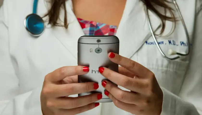 Lekarka w białym kitlu z czerwonymi paznokciami trzyma telefon. Czy pracodawca widzi kod choroby na ekranie?