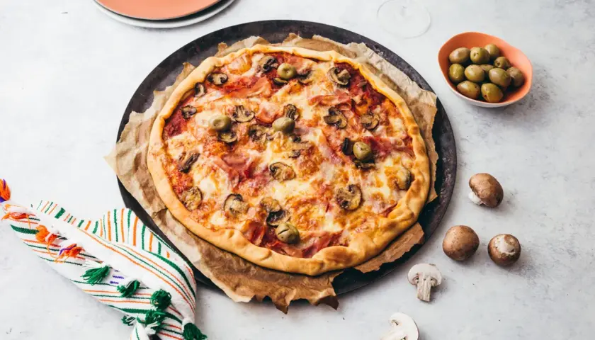 Une délicieuse pizza reine, garnie de jambon, champignons et olives, prête à être dégustée.