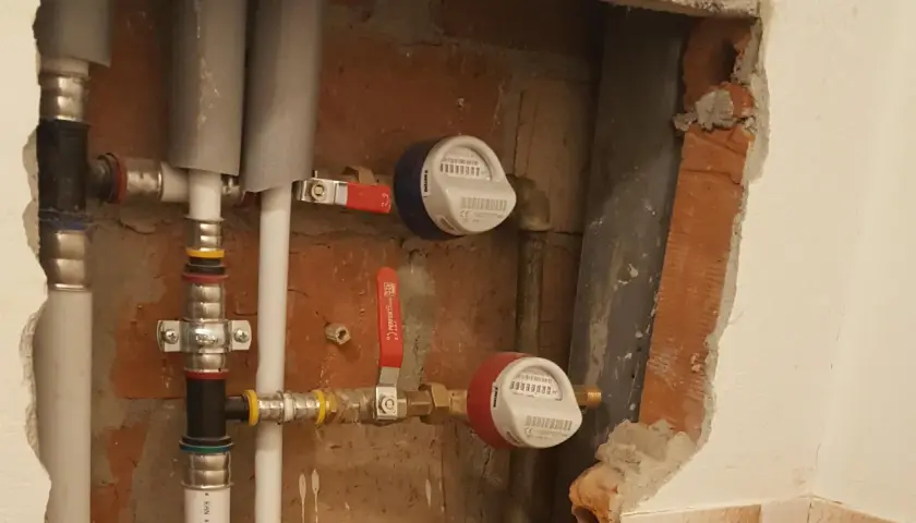 Instalacja wodna z dwoma licznikami i czerwonym zaworem.