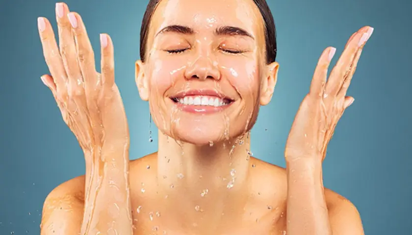 Donna sorridente con acqua sul viso e mani. L'acqua micellare serve per una pulizia delicata e rinfrescante.
