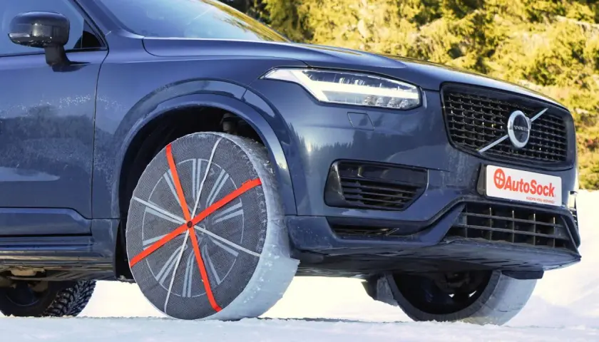 Un coche oscuro con cadenas textiles en la rueda delantera, listo para circular sobre nieve o hielo.
