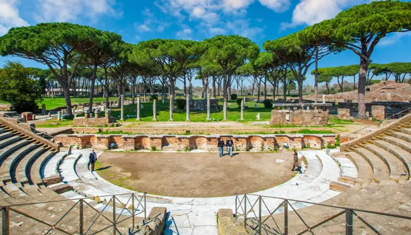 Antico teatro romano a Ostia Antica, Roma, con pini marittimi che incorniciano le rovine.