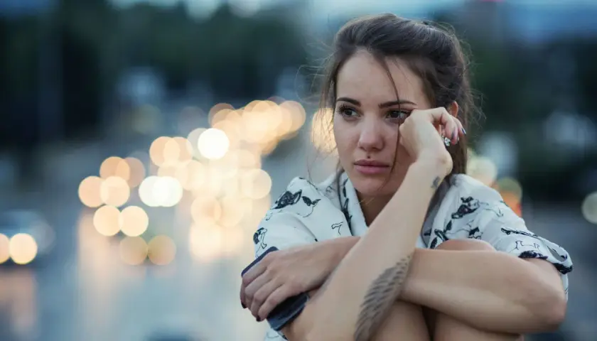 Giovane donna pensierosa, con luci sfocate sullo sfondo, sembra voler rimuovere ricordi traumatici.