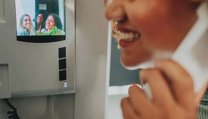 Instalación de telefonillos: mujer sonríe mientras habla por el intercomunicador, viendo a sus amigas en la pantalla.