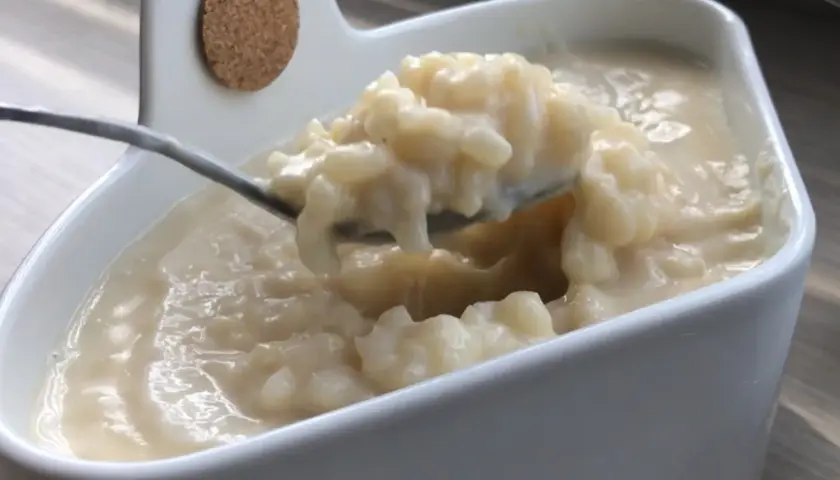 Cuillère prélevant une portion crémeuse de riz au lait dans un bol blanc.