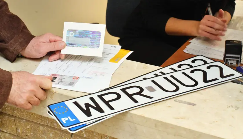 Ręce klienta pokazują dokumenty i nowe tablice rejestracyjne WPR UU22, gotowe do odbioru po załatwieniu formalności.
