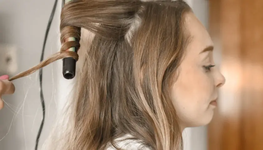 Creando peinados fáciles y rápidos: una mano riza el cabello de una mujer con una plancha.