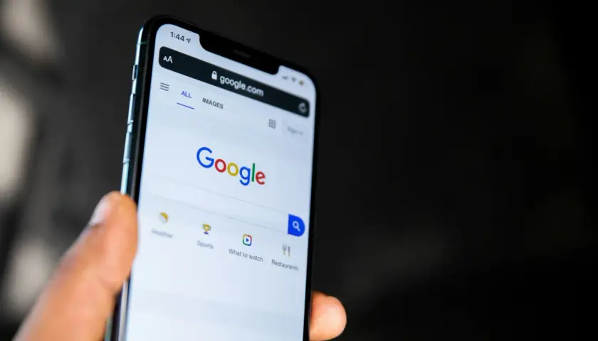 Dłoń trzyma smartfon z otwartą stroną Google. Widać pasek wyszukiwania i opcje takie jak pogoda, sport, filmy, restauracje, idealne do odkrywania treści w Google Discover.