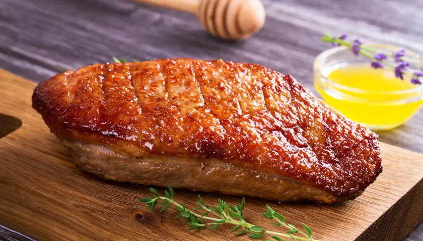 Un magret de canard au barbecue, la peau croustillante et dorée, prêt à être dégusté avec une touche de miel et de thym.