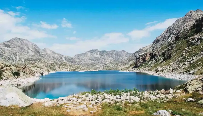 Un lago azul profundo en la vall fosca que ver, rodeado de montañas rocosas y cielo azul con nubes.