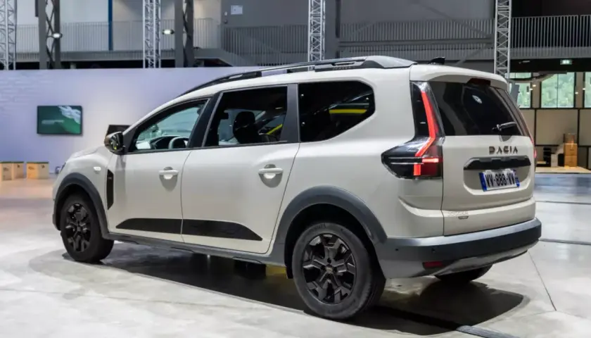 Biały samochód Dacia Jogger widziany z boku, z tyłu, na tle hali wystawowej.