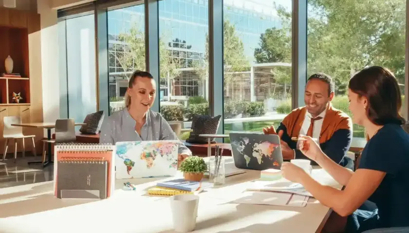 Persone che collaborano in un ufficio moderno, con laptop decorati con mappe del mondo. Una descrizione di una persona in inglese.