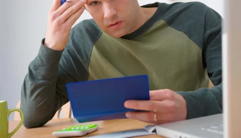 Homme pensif, calculatrice, tasse verte, ordinateur portable. Il se demande combien de temps garder chéquier.
